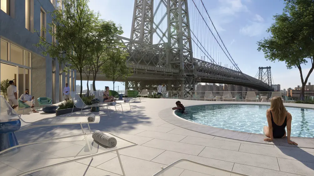 Outdoor pool deck with lounge chairs and landscaping beneath the Williamsburg Bridge.