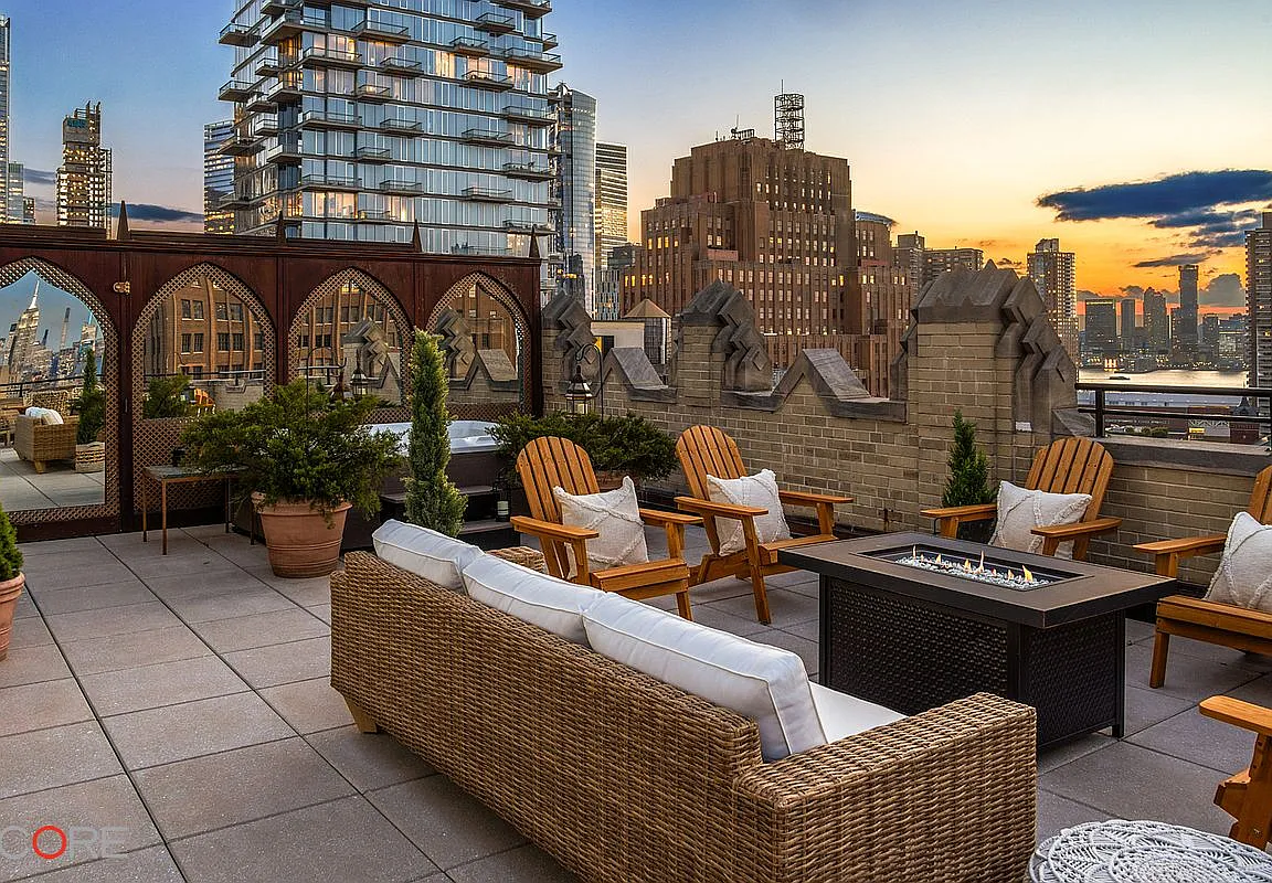 Manhattan rooftop terrace with wicker seating, a fire pit, and a city skyline at dusk.