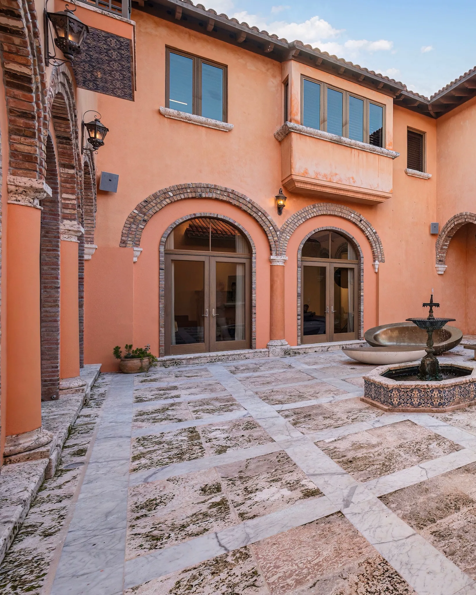 Mediterranean-style home courtyard with brick-trimmed arches, stone paving, and a fountain.