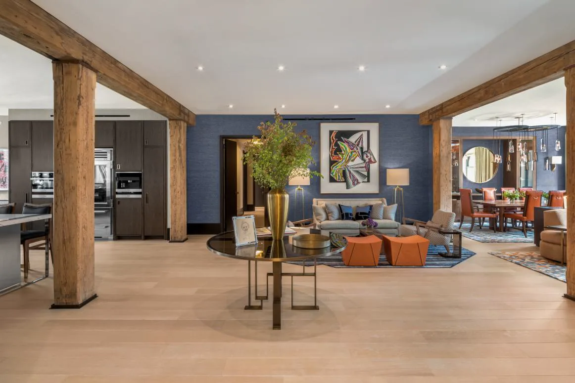 Furnished loft living room with exposed timber beams, blue accent wall, colorful artwork, and orange ottomans.