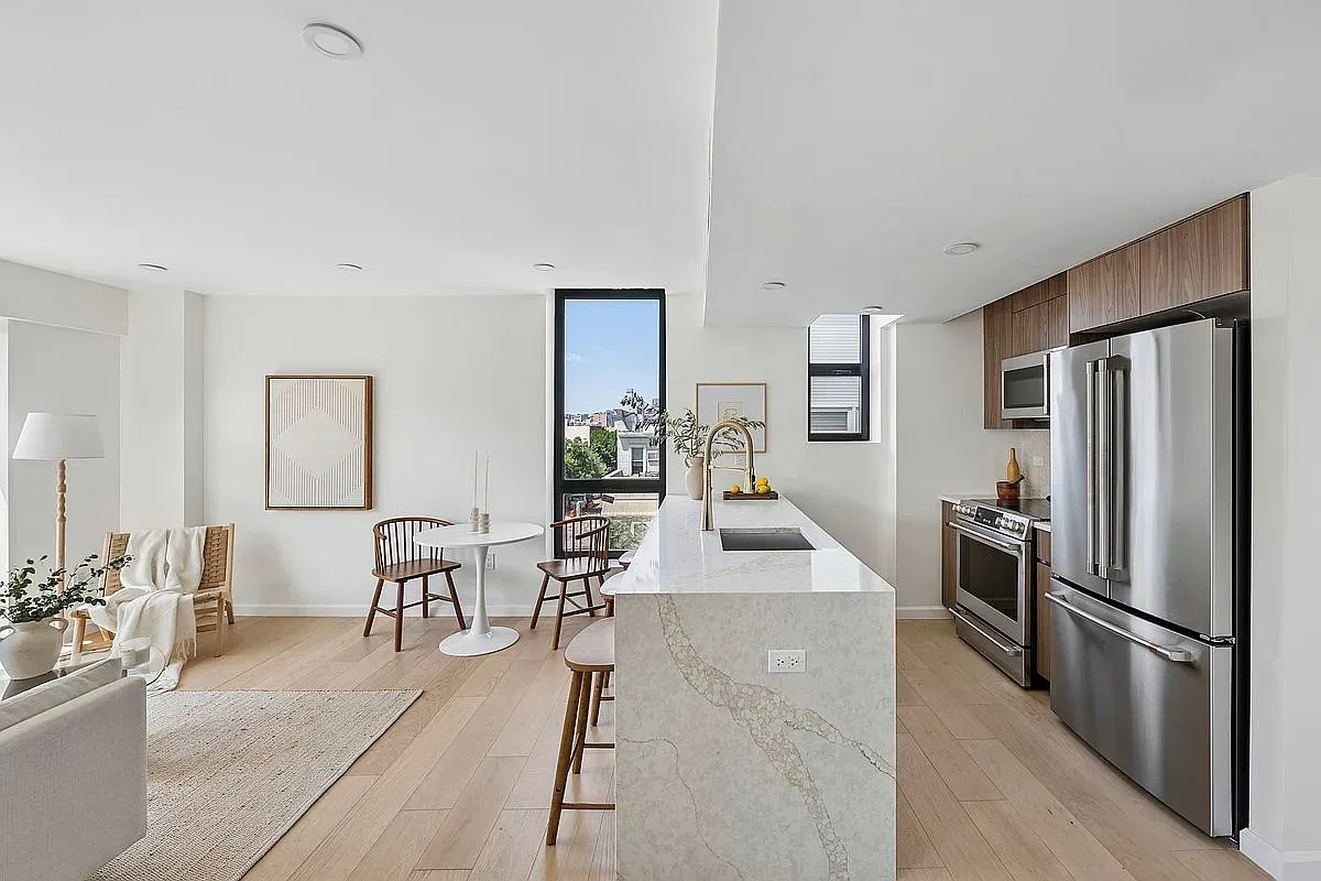 Open-plan kitchen with marble island, stainless steel appliances, and dining nook overlooking Brooklyn rooftops.