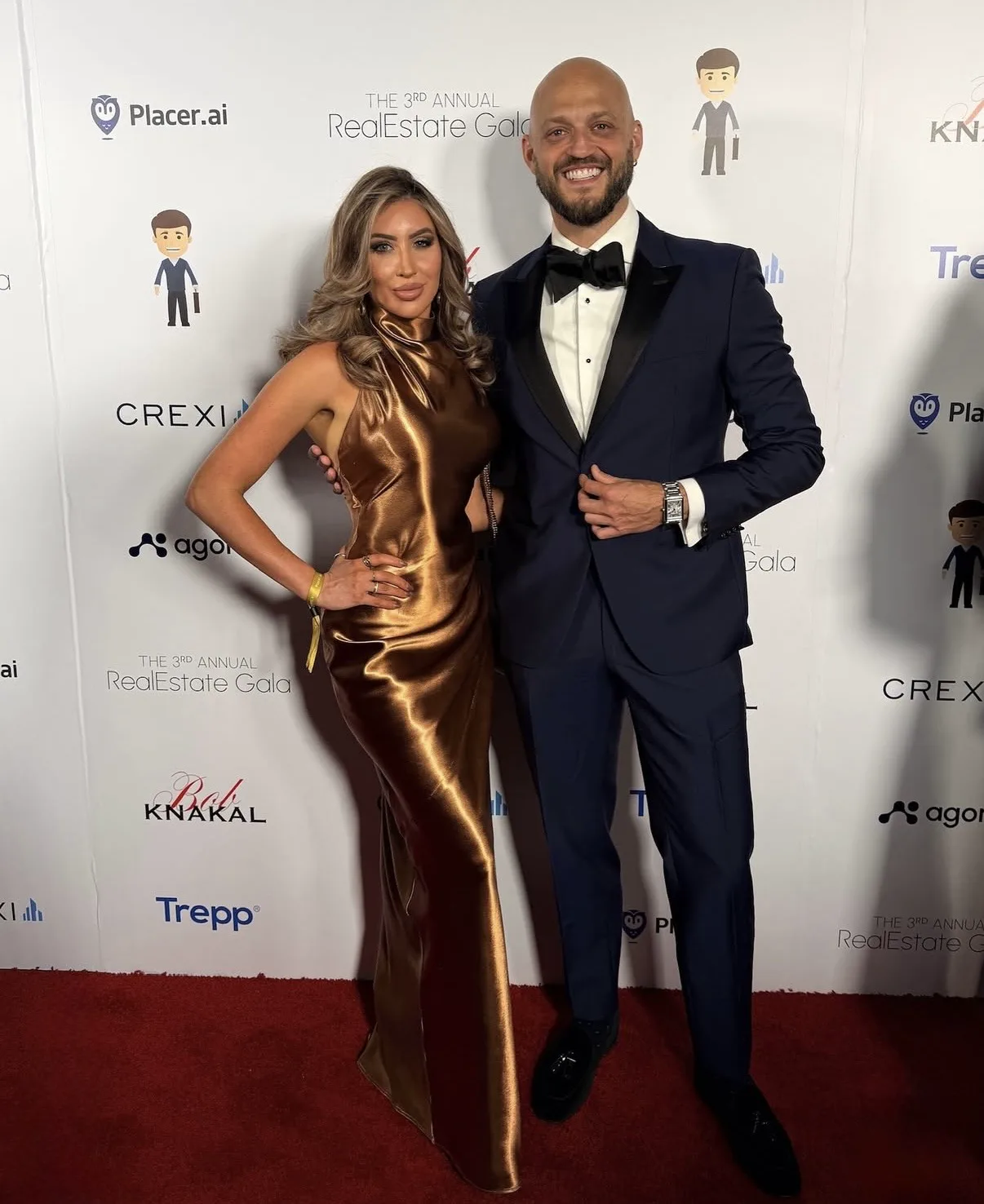 Woman in a bronze gown and man in tuxedo pose at the RealEstate Gala.