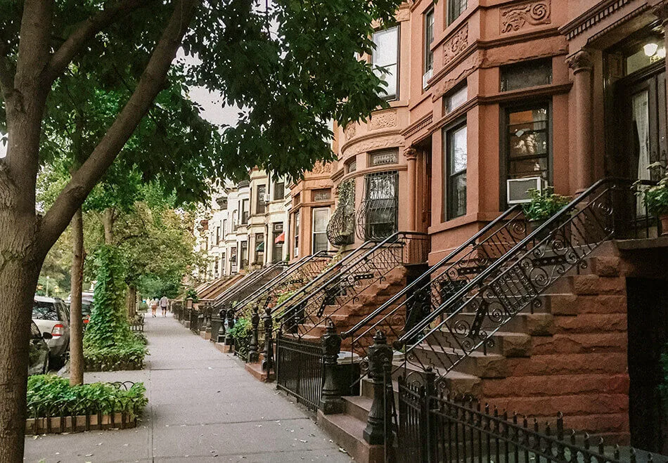 Brooklyn brownstones with ornate facades and iron-railed stoops beneath leafy street trees.
