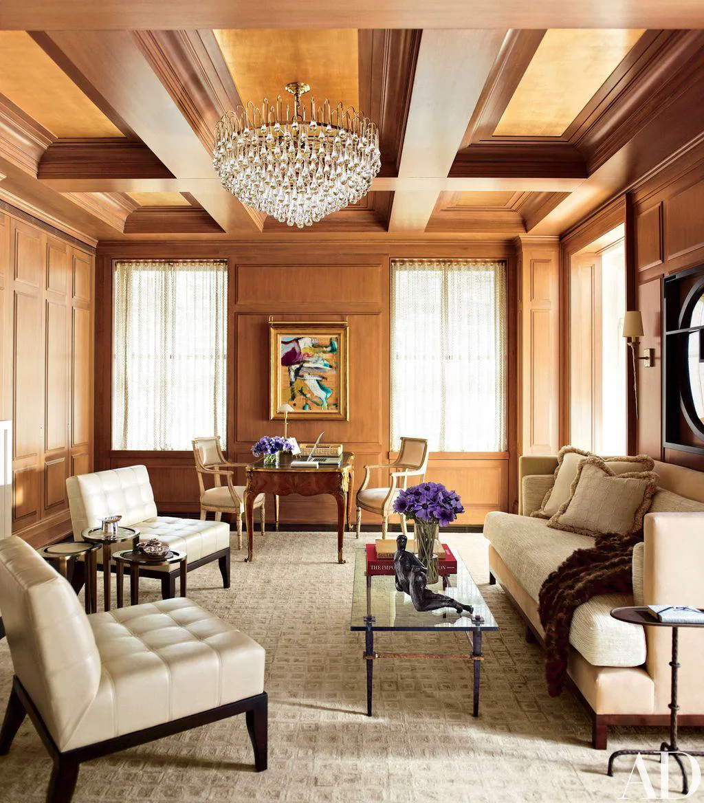 Wood-paneled living room with a crystal chandelier, cream sofas, and a glass coffee table.