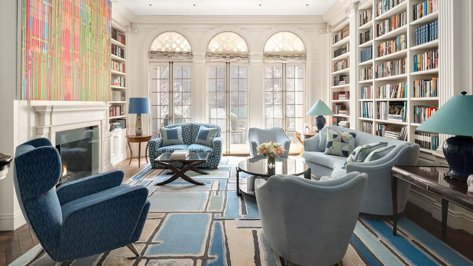 Elegant living room with arched windows, built-in bookshelves, fireplace, and blue seating.