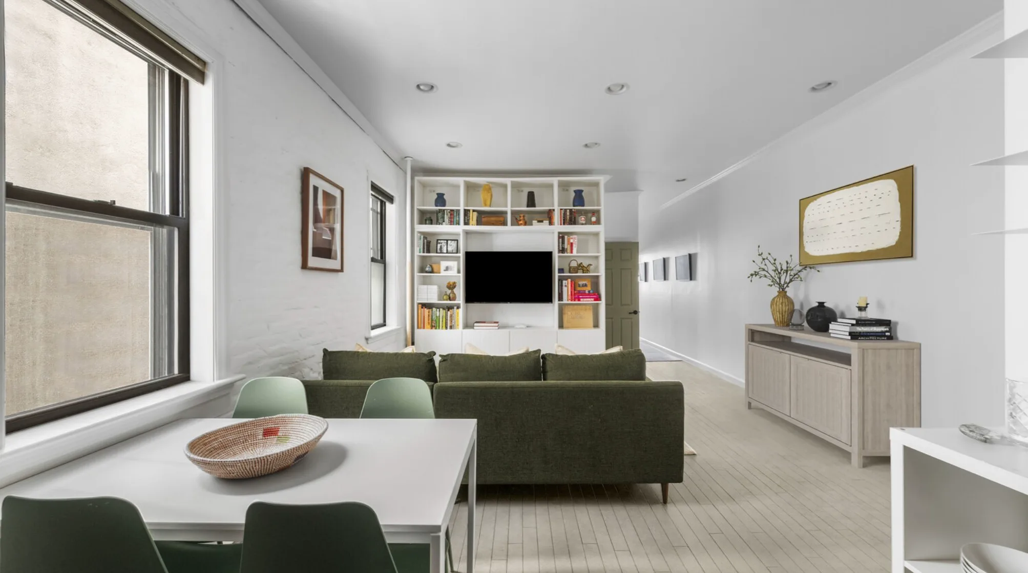 Open-plan living and dining room with large windows, a dark green sofa, and built-in bookshelves.