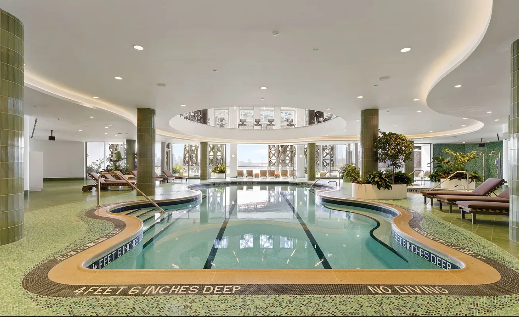 Indoor pool with curved edges, tiled surround, lounge chairs, and large windows.