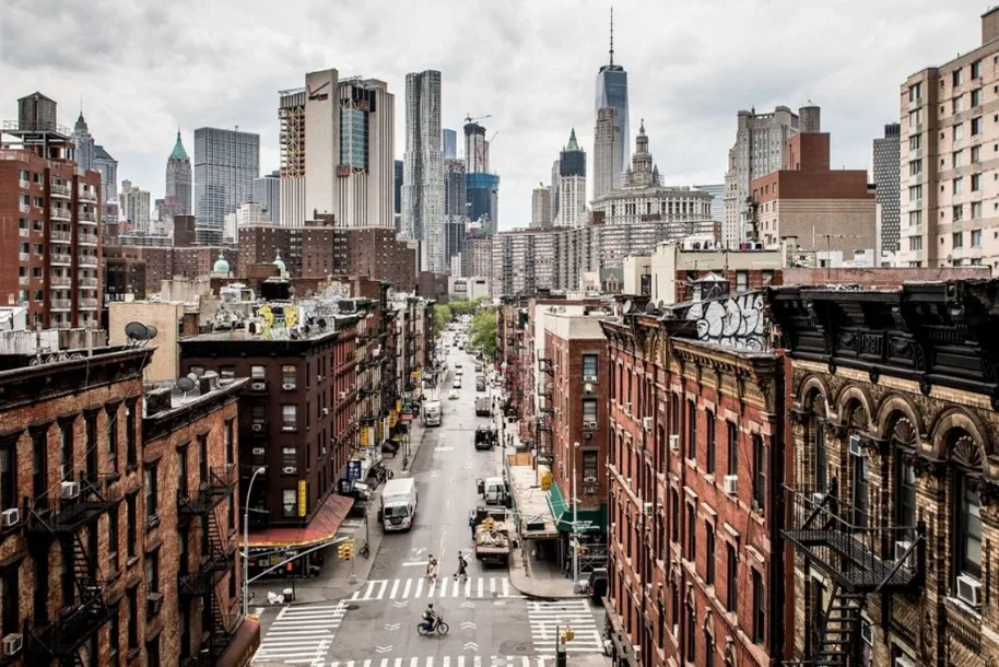 Manhattan street lined with brick buildings, with One World Trade Center rising in the distant skyline.