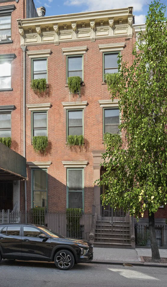 Red-brick townhouse with an ornate cornice, leafy window boxes, and a tree along the sidewalk.