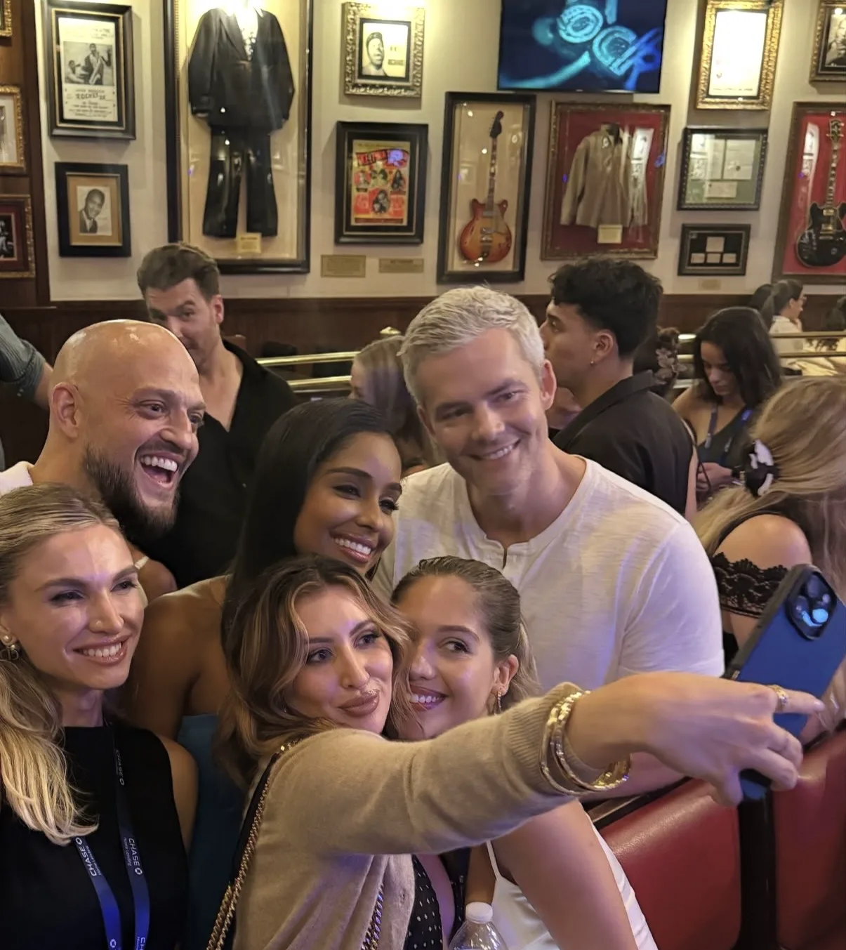 A group of adults smiles for a selfie in a crowded restaurant lined with music memorabilia.