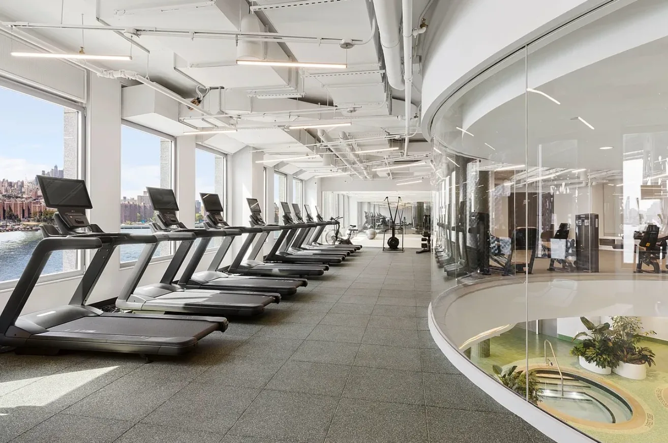 Waterfront fitness center with treadmills facing large windows and a curved glass wall overlooking the pool below.